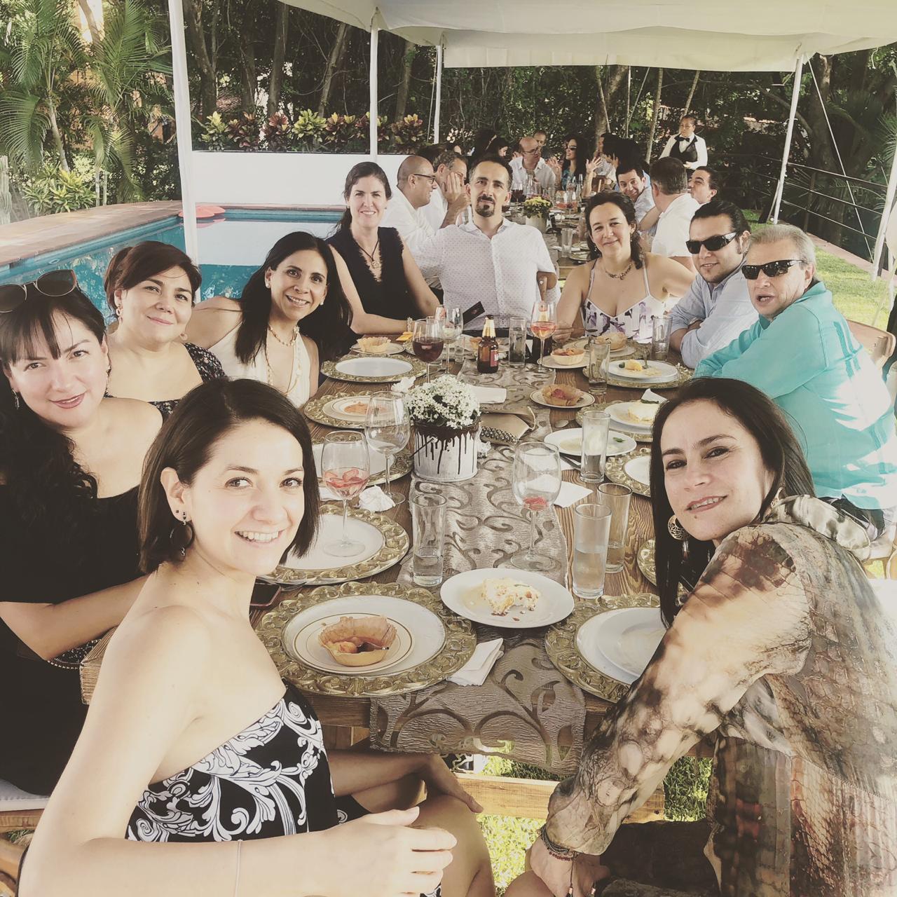 Mesa larga junto a la alberca con familia y amigos en sobremesa